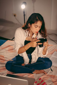 Young woman using mobile phone while sitting on bed at home