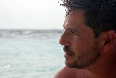 Portrait of shirtless man looking away at beach