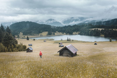 Rear view of man walking on grassy field against cloudy sky