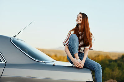 Portrait of woman sitting on car against sky