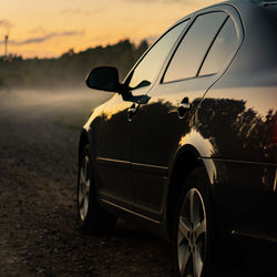 Car on road amidst field against sky during sunset