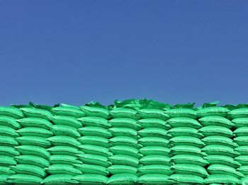 Low angle view of green stacked sacks against clear blue sky