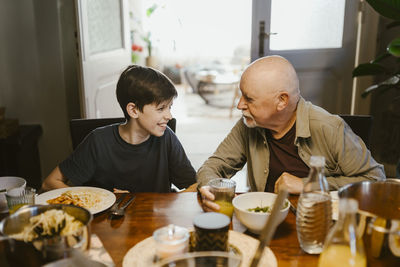 Senior man talking with grandson while sitting at dining table in home