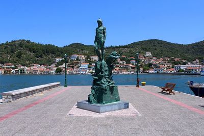 Statue by sea against clear blue sky