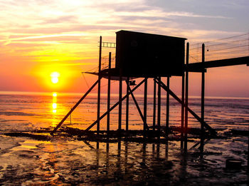 Silhouette built structure on beach against sky during sunset