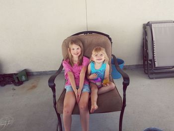 Portrait of smiling sisters sitting on chair at home