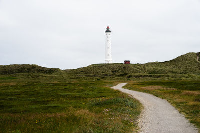 Lighthouse by street amidst buildings against sky