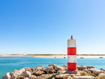 Lighthouse by sea against clear blue sky