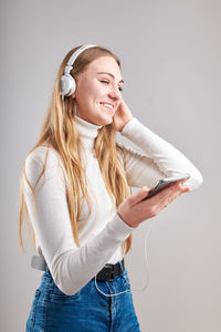 Smiling teenage girl holding mobile phone listening music against gray background