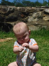 Baby boy playing with grass while sitting at field