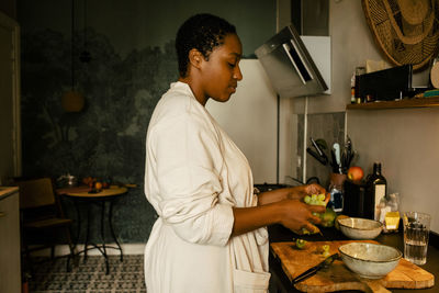 Side view of young woman with grapes at kitchen counter