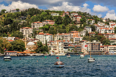 Sailboats in sea by townscape against sky