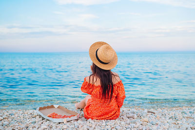 Rear view of woman wearing hat sitting at beach