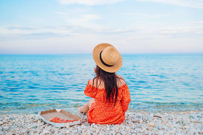 Woman wearing hat looking at sea against sky
