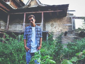 Low angle portrait of young man wearing sunglasses while standing against house