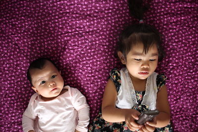 Directly above shot of cute brother and sister lying on purple blanket