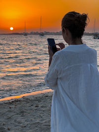 Rear view of woman standing at beach during sunset