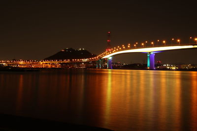 Illuminated bridge over river against sky at night