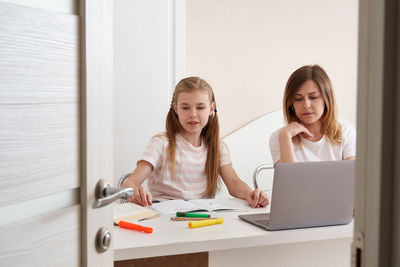 Mother and daughter sitting by desk at home