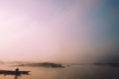 Silhouette fisherman in boat on river during foggy weather