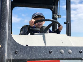 Low angle view of boy holding steering wheel of vehicle against sky