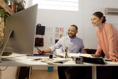 Happy male illustrator discussing with colleague at desk in creative office