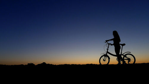 Silhouette person riding bicycle on field against clear sky