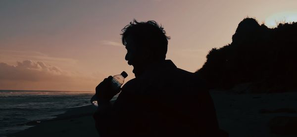 Silhouette man standing at beach against sky during sunset