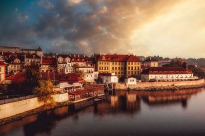 Buildings by river against sky in town at sunset