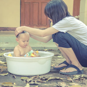 Mother cleaning boy sitting in bathtub outdoors