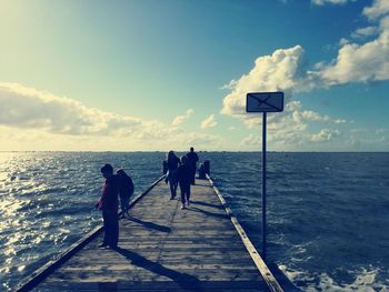 Rear view of people walking on sea against sky