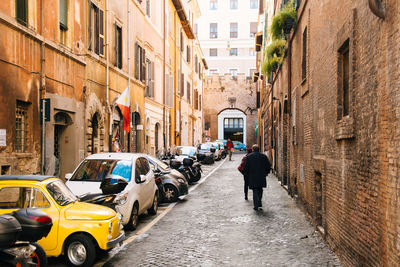 Rear view of man walking on street amidst buildings