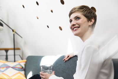 Smiling woman holding glass of water on couch