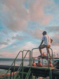 Rear view of man standing on railing against sea