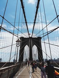 People walking on suspension bridge against sky