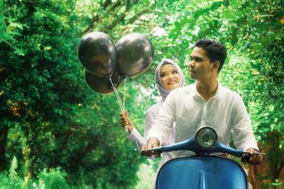 People riding on motor scooter with balloons amidst trees