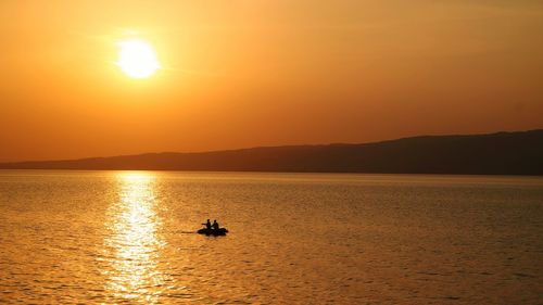 Silhouette people in boat on sea against sky during sunset