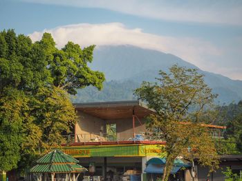 Trees and houses by mountains against sky