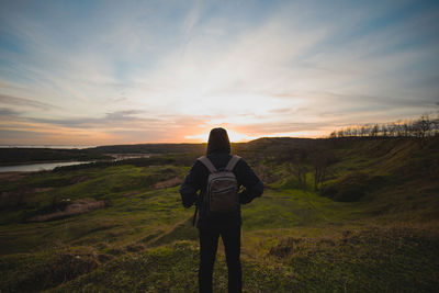 Rear view of man standing on landscape against sky during sunset
