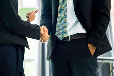 Midsection of business people giving handshake while standing in office