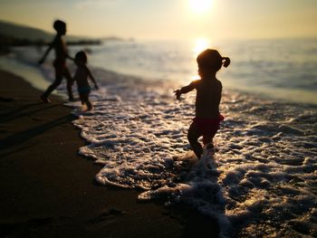 Rear view of people on beach against sky during sunset