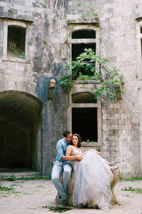 Full length of man and woman sitting in front of historic building