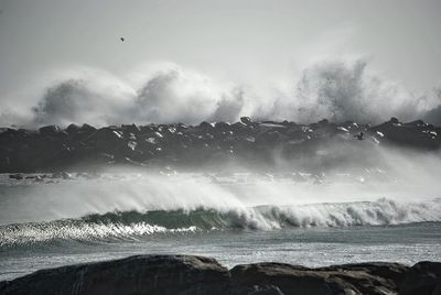 Waves splashing on groyne in sea against sky