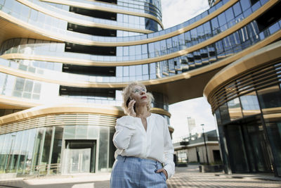 Senior businesswoman talking on mobile phone in front of office building