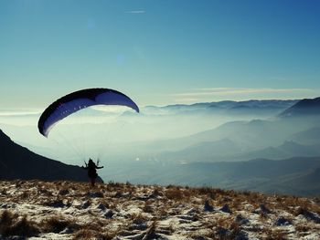 Person paragliding over mountains against sky
