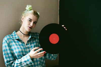 Portrait of young woman holding vinyl record while standing at home