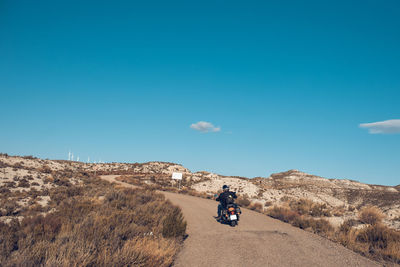 Man riding motorcycle on landscape against blue sky