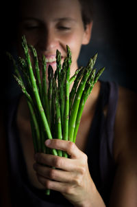 Close-up of smiling woman holding asparagus at home