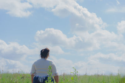 Rear view of young woman standing on grassy field against cloudy sky