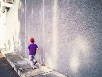 Rear view of boy walking on footpath by wall